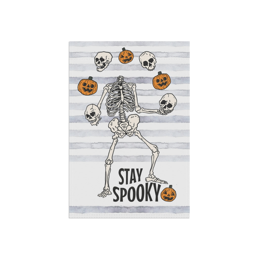 garden flag with dancing skeletons juggling pumpkins. The words on the bottom of the flag say stay spooky.